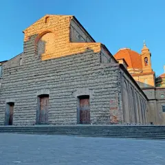 La Basilica di San Lorenzo a Firenze, con la sua facciata in pietra grezza e la cupola arancione, illuminata dal sole del tramonto.