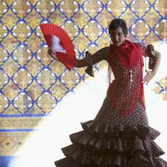Tancerka w hiszpańskim stroju flamenco, z wachlarzem w dłoni, na tle zdobionej kafelkami ściany.