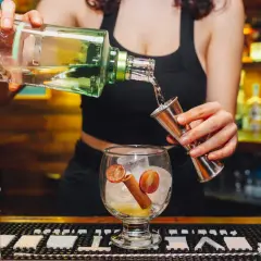 Barback nalewa alkohol z butelki do jiggera, przygotowując drinka z lodem, winogronem i cynamonem.