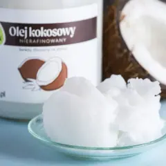 Olej kokosowy nierafinowany na talerzyku, obok słoika i połówki kokosa. Idealny do smażenia i pieczenia.