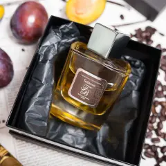 Perfumy "Tobacco" by Franck Boclet w eleganckim flakonie, otoczone śliwkami, kawą i cygarem.