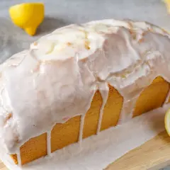 Saftiger zitronenkuchen in Kastenform, überzogen mit süßem Zuckerguss. Ein Zitronenstück liegt daneben.