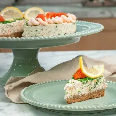 En läcker laxtårta på kavring, dekorerad med räkor, rom och citron. En bit serveras på en mintgrön tallrik.