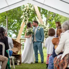 Un couple s'embrasse lors de leur baptême civil, entouré de leurs proches sous une tente décorée de fleurs.