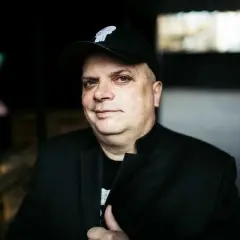 Krzysztof Skiba w czapce z daszkiem i czarnej marynarce, jakby przygotowywał się do wykonania swoich kultowych utworów.