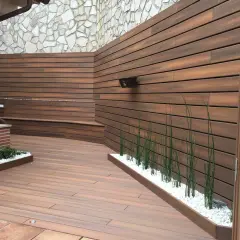 Moderna zona barbacoa exterior con tarima de madera, bancos integrados y vegetación.
