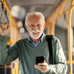 Uśmiechnięty starszy pan w autobusie, korzystający z ulgi dla emerytów w Wałbrzychu. Trzyma telefon i poręcz.