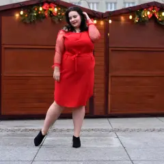 Kobieta w czerwonej sukience prezentuje eleganckie komplety damskie ze spodniami XXL, pozując na tle świątecznych straganów.
