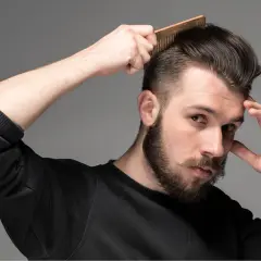 Man med skägg och mustasch kammar sitt hår som har en snygg taper fade.