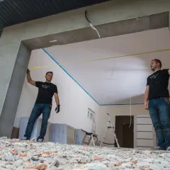 Dwóch mężczyzn mierzy otwór bramy garażowej. Precyzyjna obróbka otworu to klucz do idealnego montażu.
