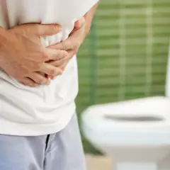 Mann hält sich den Bauch, deutet auf mögliche Harnverhalt Symptome. Im Hintergrund eine Toilette.