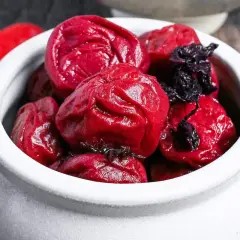 A white ceramic bowl filled with glistening, deep red umeboshi plums, ready for a delicious umeboshi recipe.