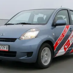 Szary Daihatsu Sirion z napisem "AUTO CLUB DAIHATSU" na boku, jadący po drodze.
