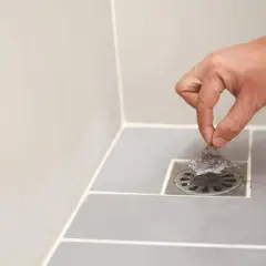 Main d'une personne retirant des cheveux du siphon pour déboucher la douche.