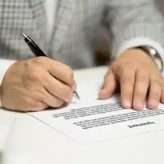 Mężczyzna w garniturze podpisuje umowę kredytową, składając ważny podpis na dokumencie.