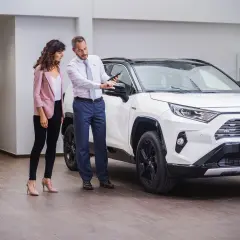 Sprzedawca pokazuje klientce detale białej Toyoty RAV4 na tablecie. To pewne auto dla wymagających.
