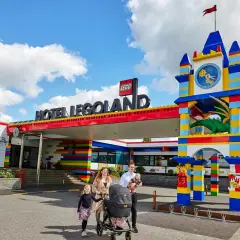 Rodzina z wózkiem spacerowym przed kolorowym hotelem Legoland Kopenhaga. Smoczy zegar i wejście z klocków LEGO.