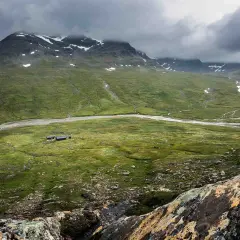 Grönskande fjällandskap med en slingrande flod och små stugor. En vy som kan vara en del av kungsleden etapper.