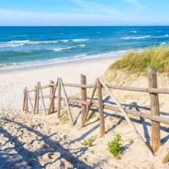 Piękna plaża w Łebie, idealne miejsce na spacer. Drewniane płotki prowadzą do morza, a trawy na wydmach dodają uroku.