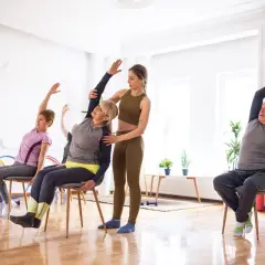 Cours de gym avec une chaise : une monitrice guide des seniors dans des étirements doux.