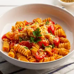Pyszny makaron z warzywami: fusilli w sosie pomidorowym z pomidorkami koktajlowymi, posypany parmezanem i natką pietruszki.