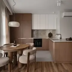 Wnętrze kuchni z drewnianymi frontami w kolorze greige, okrągłym stołem i krzesłami.