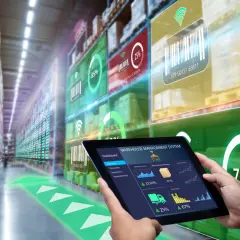 Ręce trzymają tablet z systemem zarządzania magazynem, wyświetlającym dane o zapasach i postępie. W tle widać regały magazynowe z nakładkami AR, prezentującymi **opakowania inteligentne** i ich status.