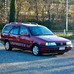 Ciemnoczerwony Fiat Tempra S.W. 4x4 z relingami dachowymi zaparkowany na tle drzew.