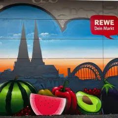 Graffiti mit Kölner Dom, Brücke und Früchten vor REWE-Logo.