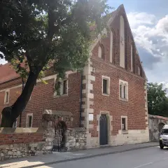 Stary ceglany budynek z kamiennymi detalami, otoczony murem i drzewem. To jedna z kazimierza wielka atrakcji, gdzie historia spotyka się z teraźniejszością.
