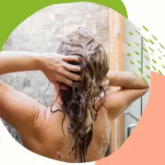 Kobieta masuje mokre włosy pod prysznicem, stosując naturalny peeling do skóry głowy.