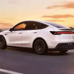 Biały Tesla Y 2025 pędzi po drodze o zachodzie słońca.