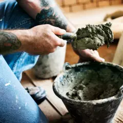 Rzemieślnik z tatuażami miesza zaprawę murarską, dbając o właściwe proporcje.