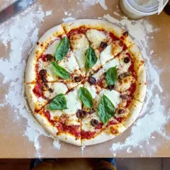 Pizza Margherita fraîchement sortie du four, avec son fromage fondant, ses olives et son basilic. Le temps de cuisson pizza four 250°C est parfait.