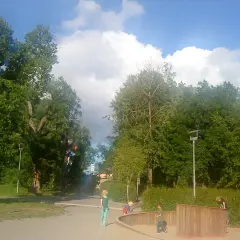 Barn leker i fruktparken Liljeholmen bland gröna träd och en blå himmel med moln.