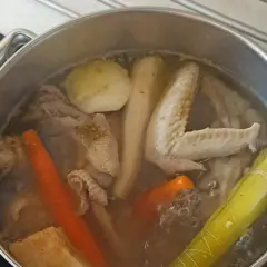 Gotowanie rosołu bez przykrycia. W garnku bulgoczą kawałki kurczaka, marchewka, por i inne warzywa.