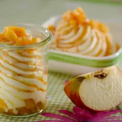 Cremige Mehlspeise mit Apfelstücken in einem Glas, daneben eine Schüssel mit derselben Leckerei und ein Apfelstück.