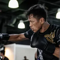 A boxer practices his form, throwing a punch at a heavy bag. His focus is intense as he trains.
