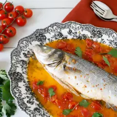 Spigola all'acqua pazza, un piatto succulento con pomodorini e prezzemolo, pronto per essere gustato.