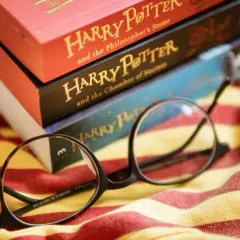 Okulary Harry'ego Pottera leżą na tle książek z serii i szalika Gryffindoru. To idealny cytat z Harrego Pottera dla każdego fana.