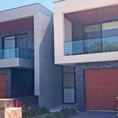 Nowoczesny dom bliźniak z drewnianymi bramami garażowymi i szklanymi balustradami balkonowymi.