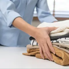 Dłoń układa stos czystych ubrań. Poznaj skuteczne sposoby, jak usunąć zapach stęchlizny z ubrań i cieszyć się świeżością.