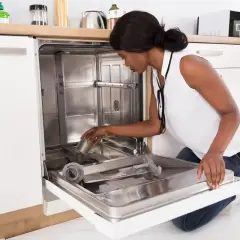 A woman is kneeling and placing a filter into a new dishwasher during its installation.