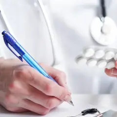 Lekarz przepisuje leki przeciwlękowe, trzymając blister tabletek i pisząc receptę.