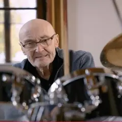 Phil Collins, legenda perkusji, siedzi przy zestawie bębnów, gotów do gry.