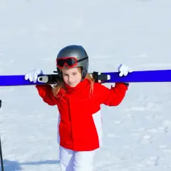 Uśmiechnięta dziewczynka w czerwonej kurtce i białych spodniach niesie narty na ramionach. Gotowa na ferie zimowe 2026 lubuskie.