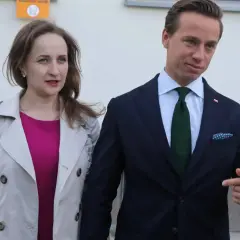 Kobieta w różowej sukience i jasnym płaszczu obok mężczyzny w granatowym garniturze.