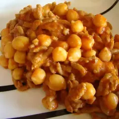 Un plato de garbanzos con carne picada, cocinado en una salsa rojiza y servido en una vajilla blanca con rayas negras.