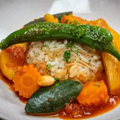 Herzhaftes Reisgericht mit viel Gemüse, darunter Karotten, Zucchini und eine grüne Chilischote, serviert in einer roten Sauce.