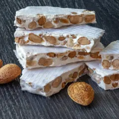 Barras de turrón, un dulce tradicional español, apiladas con almendras enteras. ¿Qué es nougat? Es este delicioso manjar.
